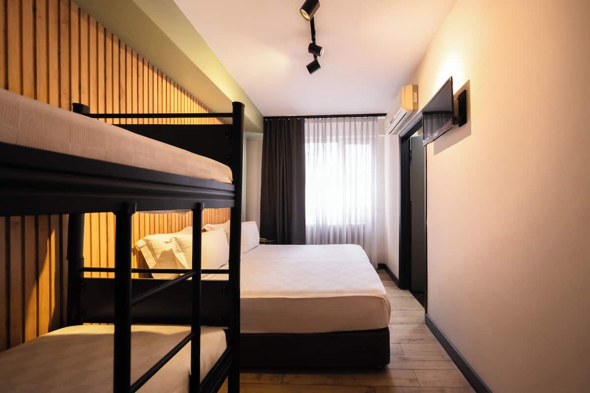 A hotel room with bunk beds, a large window with curtains, a ceiling light, and a wall-mounted TV.