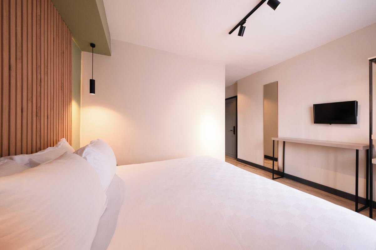 A modern hotel room with a large bed, a desk, and a TV.