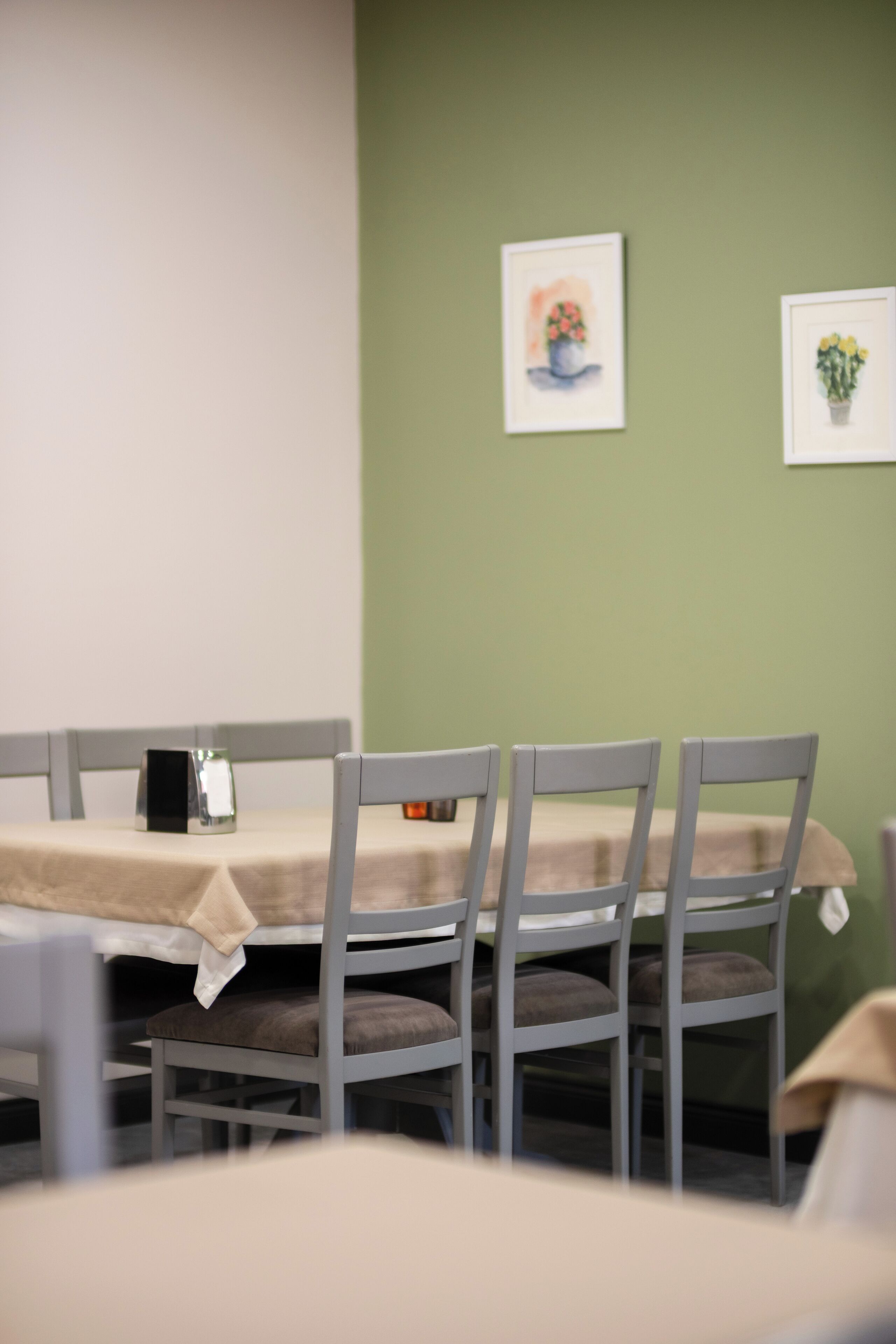 A dining area with a table set for four, grey chairs, and two framed floral artworks on the wall.