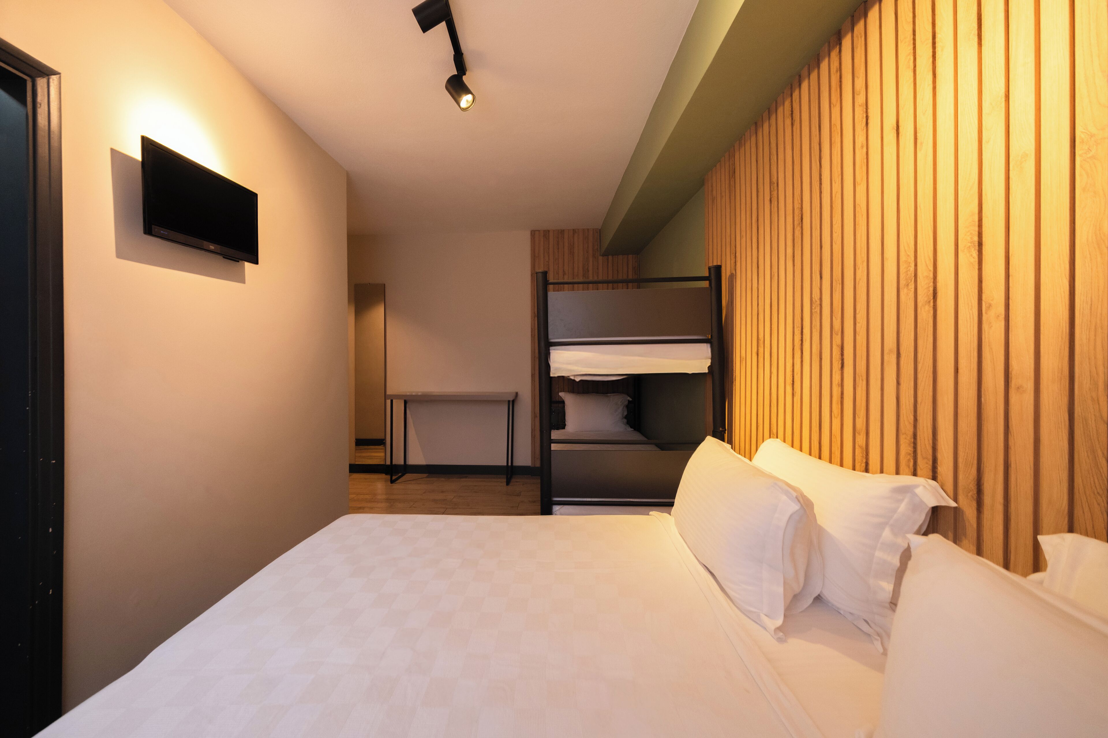Una habitación de hotel moderna con una cama litera, un televisor de pantalla plana montado en la pared y una mesita de noche.