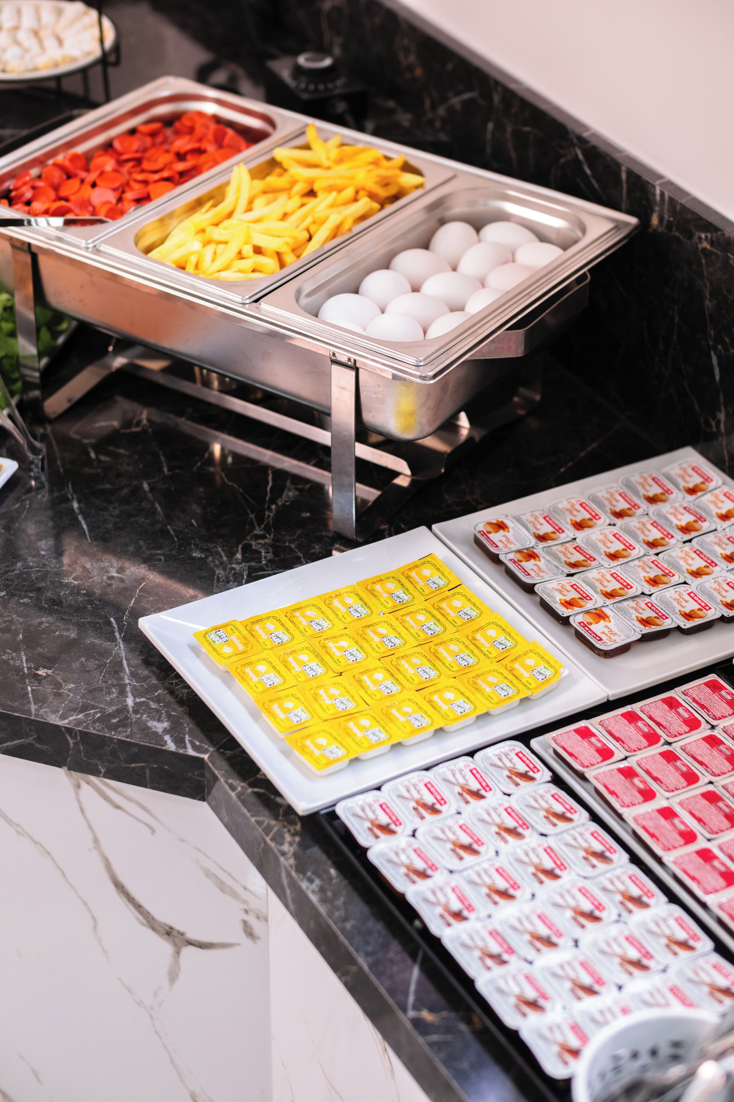 Un bufé con bandejas de comida que incluyen papas fritas, huevos y refrigerios envasados.