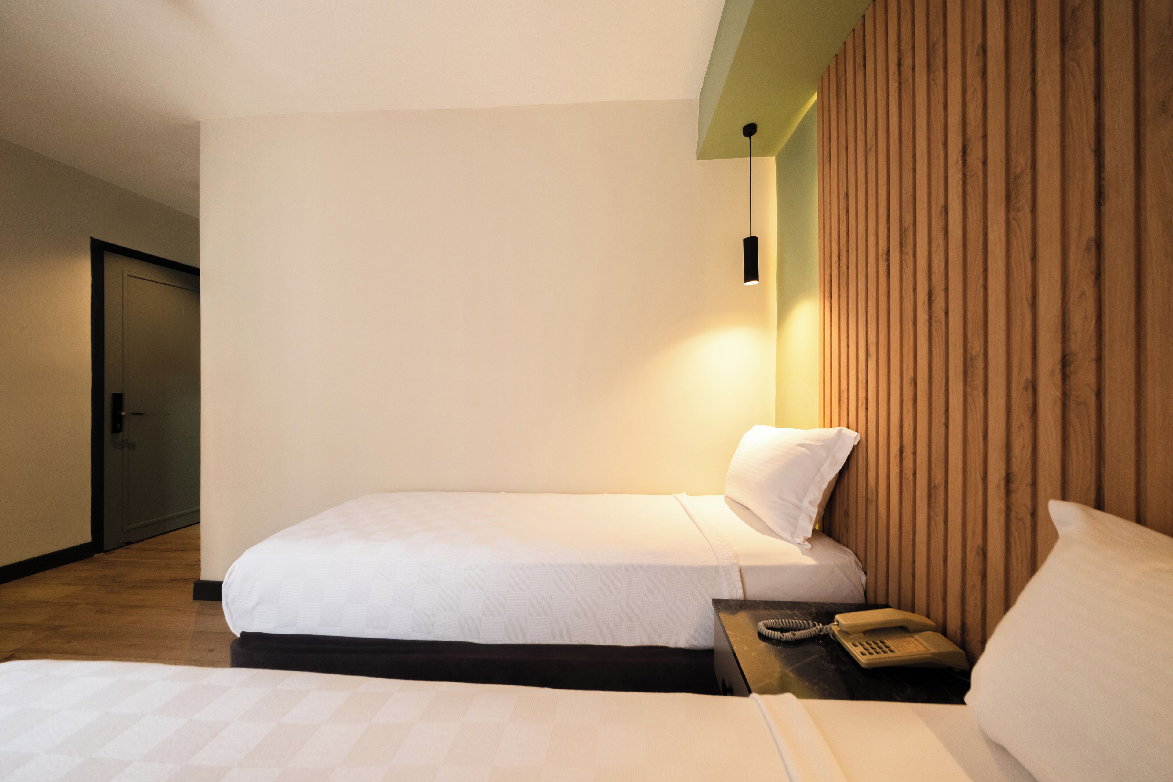 A hotel room with a bed, a bedside table with a telephone, and a wooden panel wall.