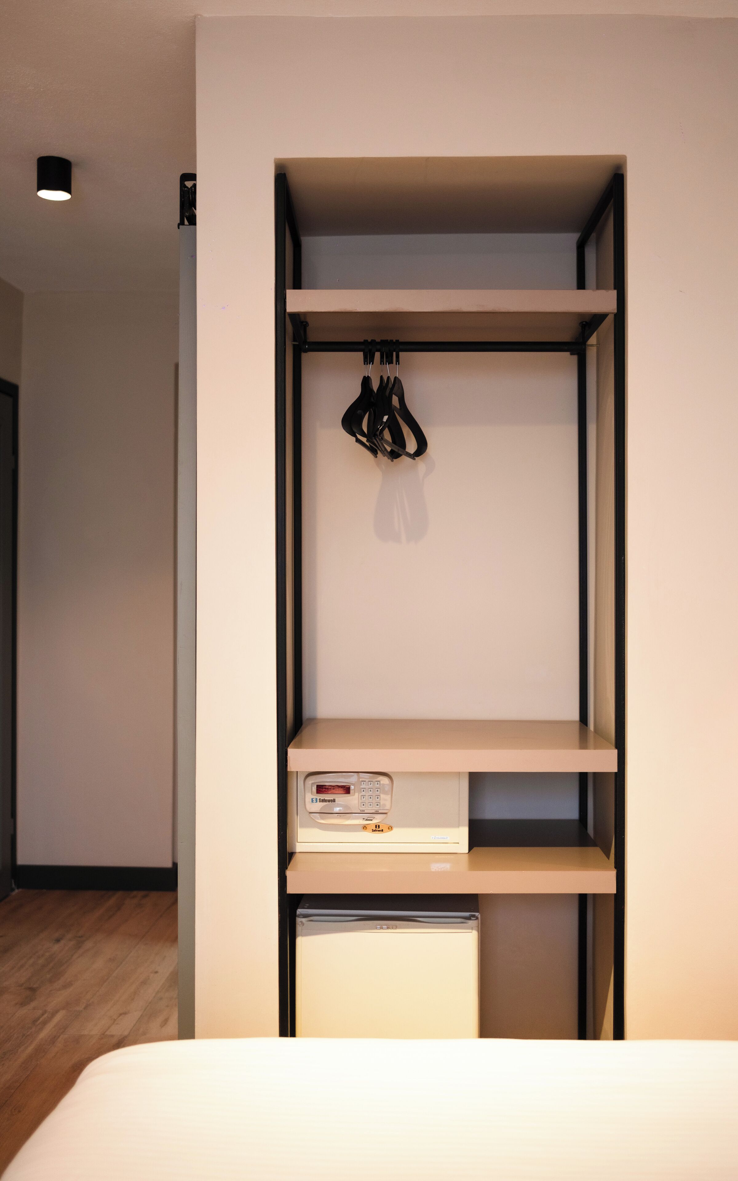 A compact room with a bed, a small desk with a computer, and a shelf with a hanging item.