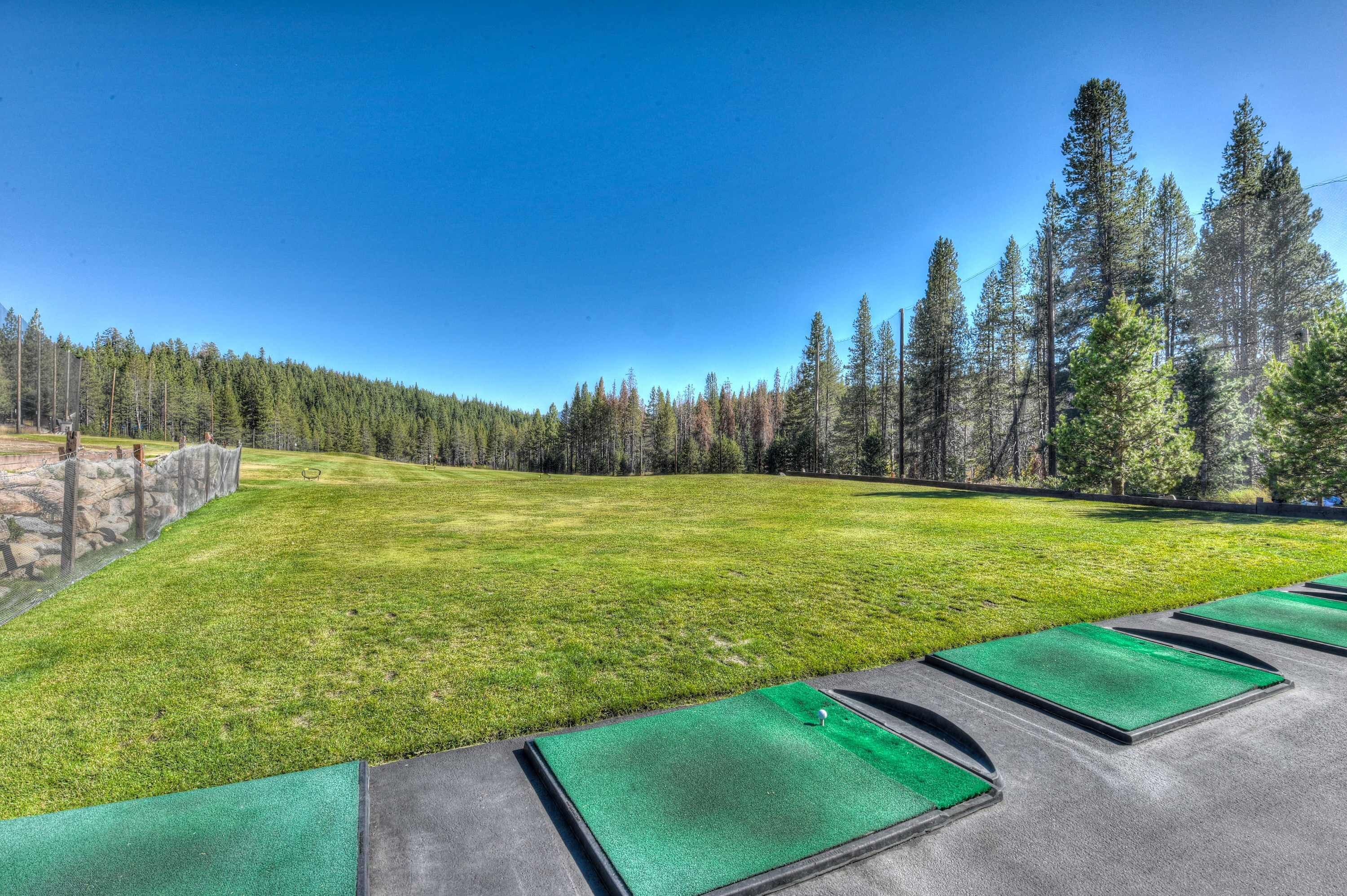 A golf course with a clear sky, a well-maintained green, and a row of tee boxes.