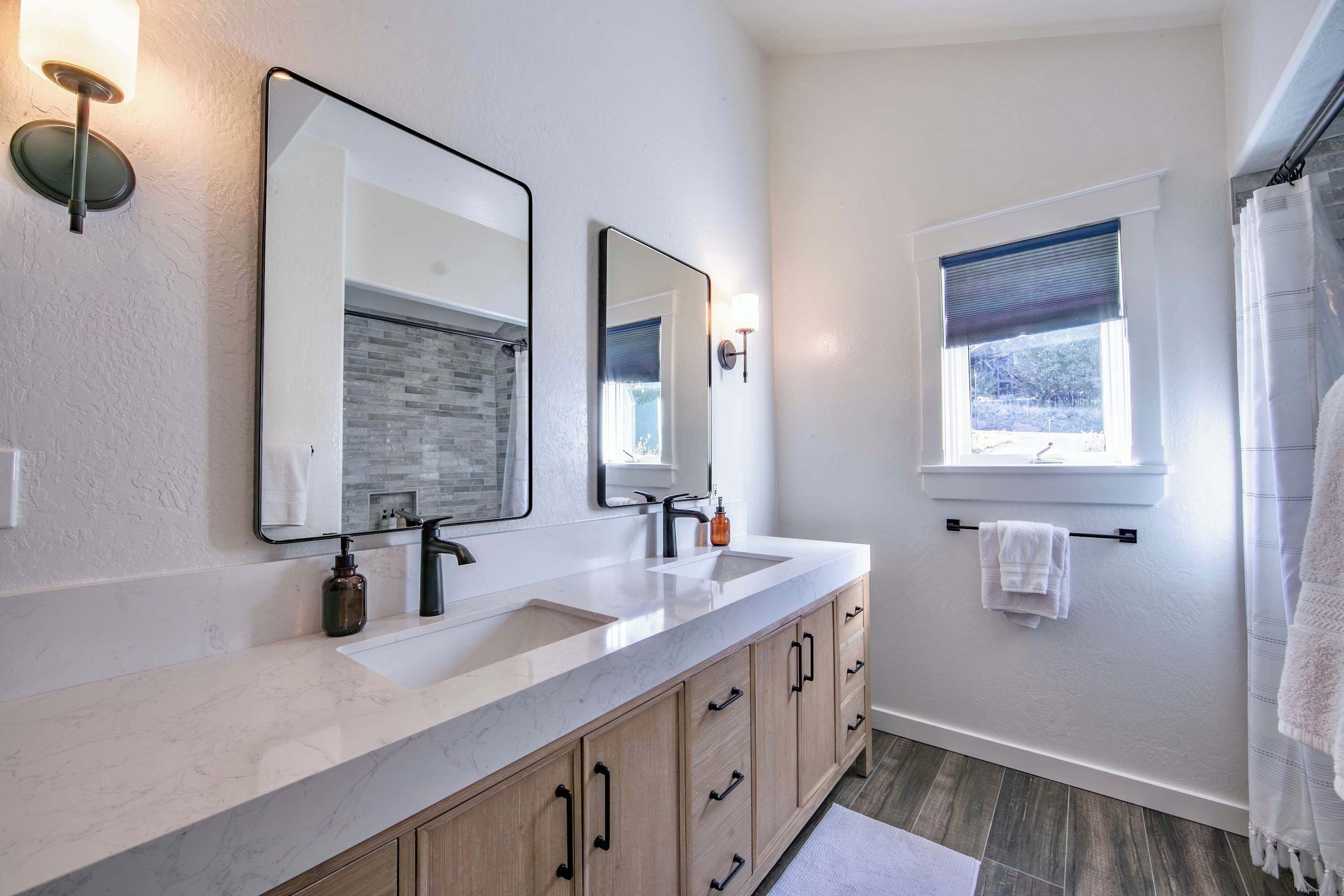 A modern bathroom with a large vanity, two mirrors, a window with a view, and a towel rack.