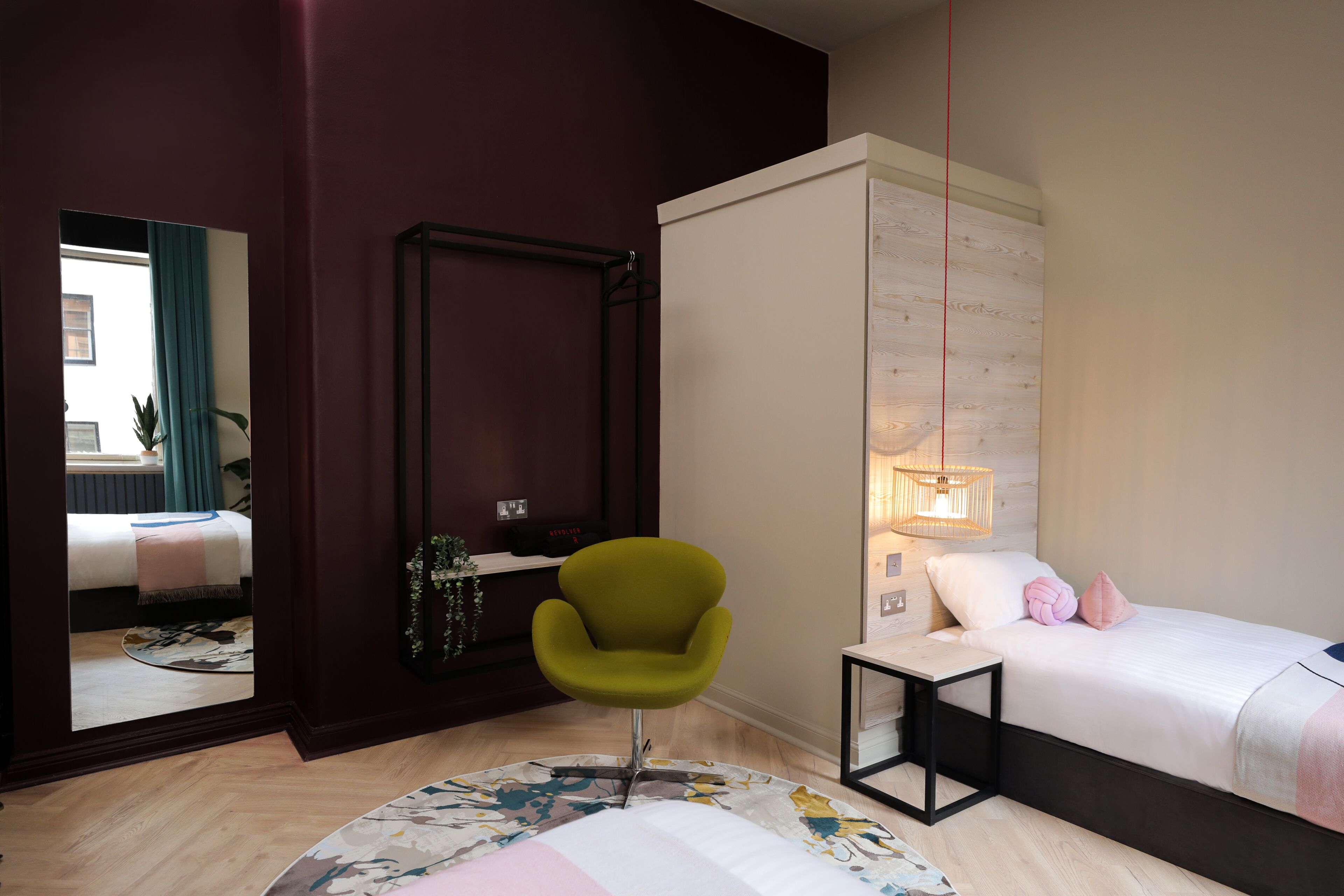 A modern bedroom with a bed, a green chair, a bedside table, and a mirror.