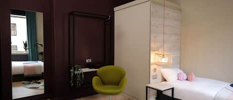 A modern bedroom with a bed, a green chair, a bedside table, and a mirror.