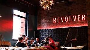 A group of people sitting on a couch in a room with a brick wall and a neon sign that reads "REVOLVER". - Revolver Glasgow (Glasgow)