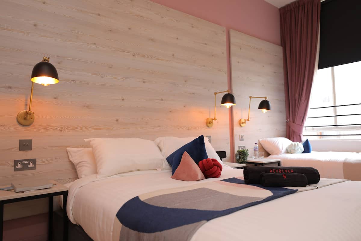 Ein Hotelzimmer mit hölzernem Kopfteil, zwei Nachttischen, einem Bett mit geometrischem Muster auf der Tagesdecke und zwei Wandlampen zum Lesen.