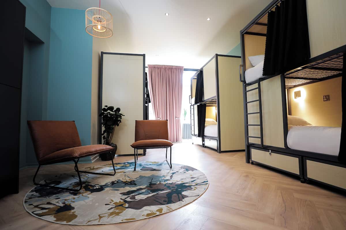 Ein modernes Hotelzimmer mit einem Etagenbett, zwei Sesseln, einem runden Teppich und einer Hängelampe.