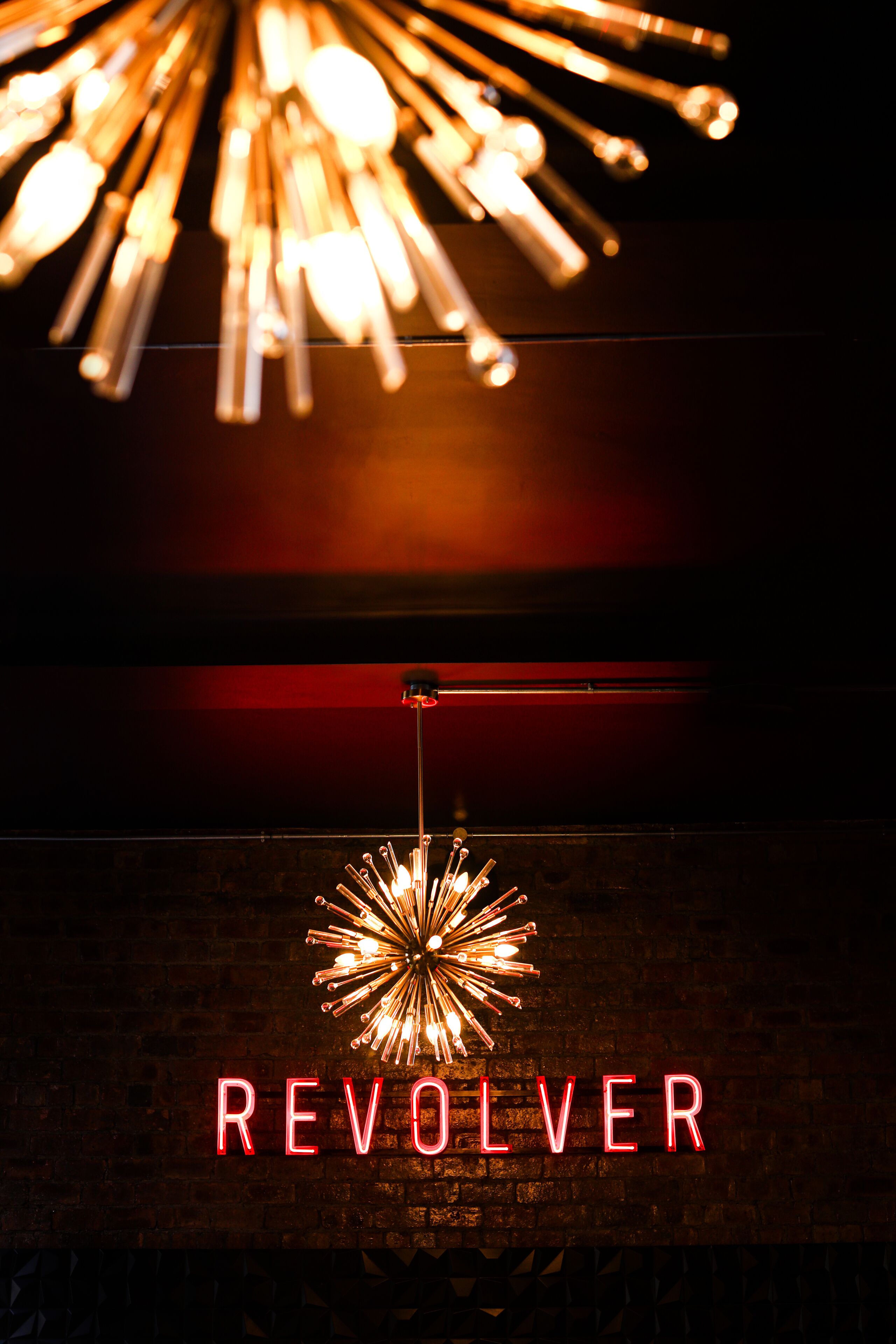 A neon sign with the word "REVOLVER" against a brick wall.