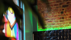 A person sitting on a leather couch with a laptop, in a room with a brick wall and a geometric patterned wall behind them. - Revolver Glasgow (Glasgow)