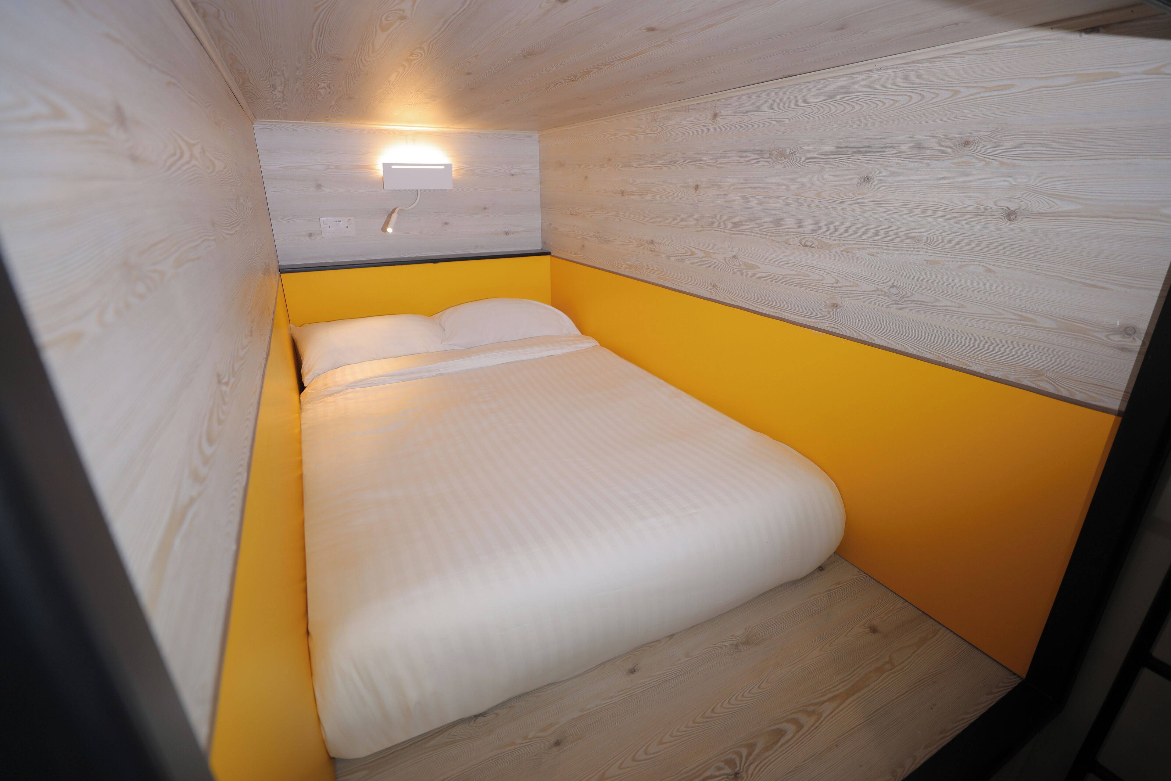 A small, cozy room with a bed, a wall-mounted light, and wooden paneling.
