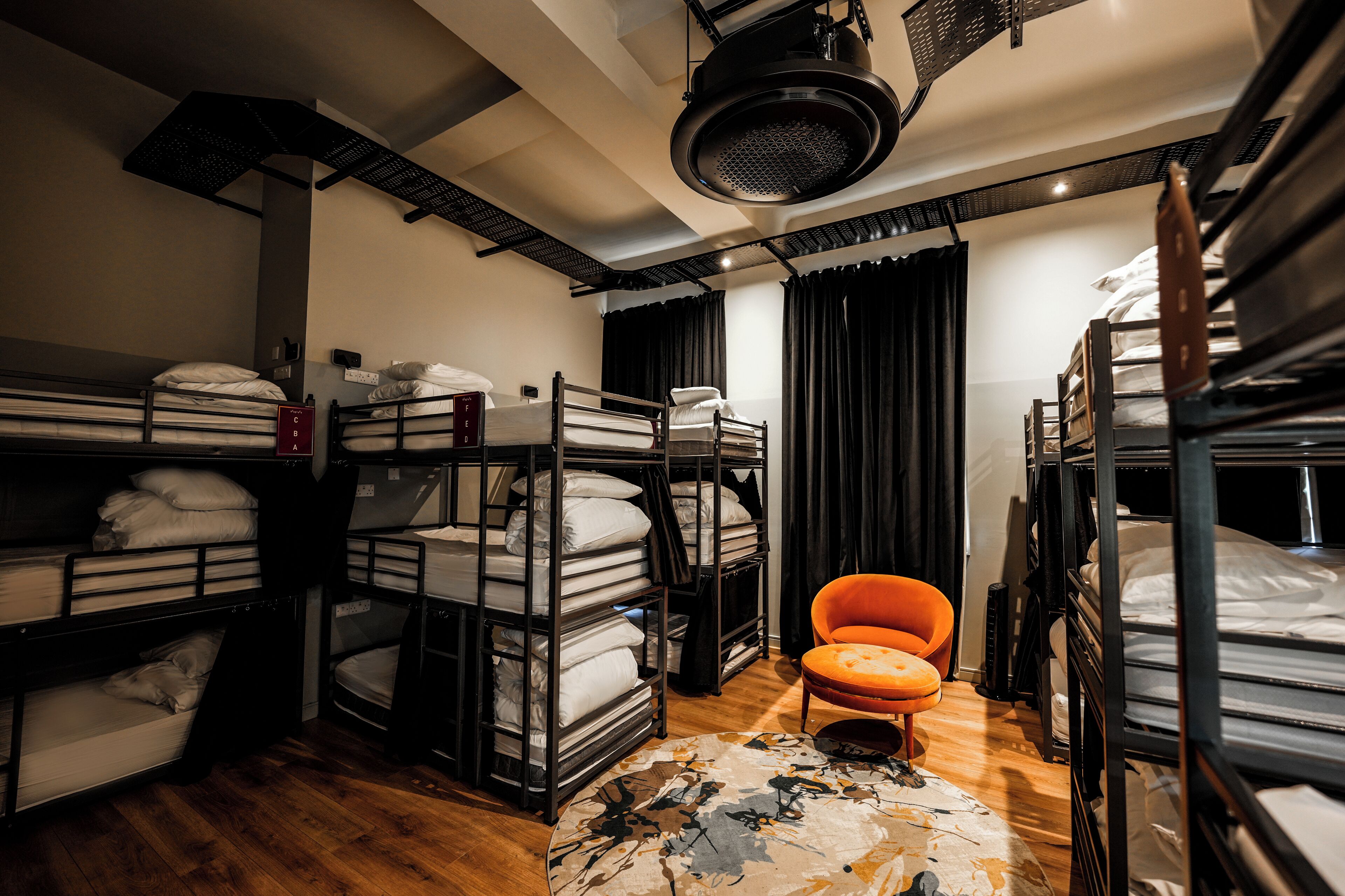 A dormitory-style room with bunk beds, a chair, and a ceiling fan.