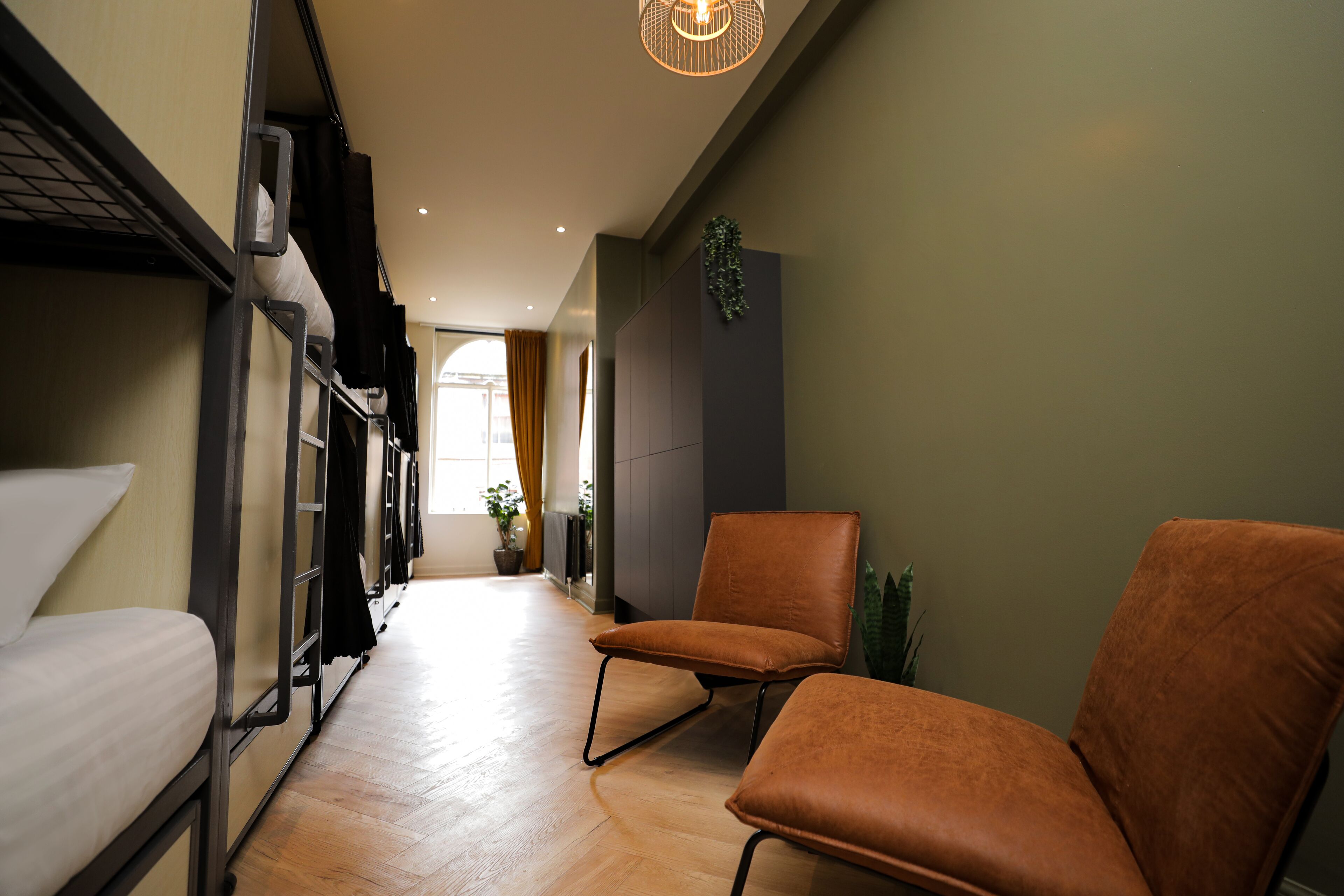 A narrow hallway with bunk beds on one side and two orange chairs on the other.