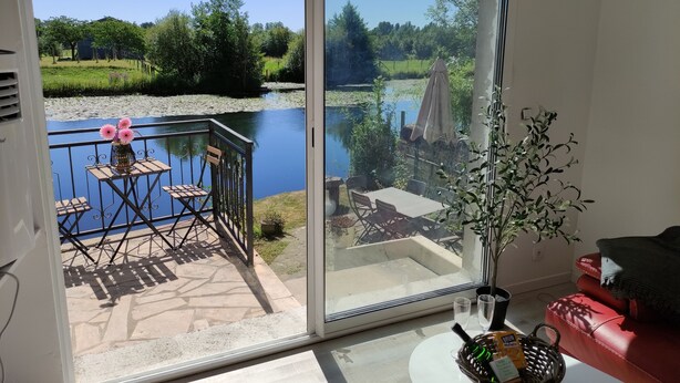 A room with a sliding glass door leading to a balcony with a table, chairs, and a vase of flowers. - Relaxation on the banks of the Loir, Gîte2 (Les Roches L'Evêque)