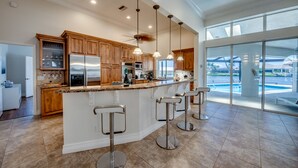 A modern kitchen with a central island, bar stools, and a view of a swimming pool.