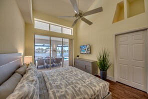A bedroom with a bed, a ceiling fan, a TV, a potted plant, and a view of a pool and outdoor seating area. - Villa Superior - great view with heated pool and spa, tiki hut & billard (Cape Coral)