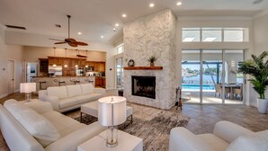 A spacious living room with a fireplace, a kitchen in the background, and a view of a pool through large windows.