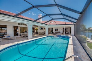 A swimming pool with a glass enclosure, lounge chairs, and a patio area with tables and chairs. - Villa Superior - great view with heated pool and spa, tiki hut & billard (Cape Coral)