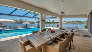 A dining area with a pool view, outdoor seating, and a ceiling fan.