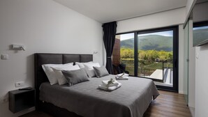 Een moderne slaapkamer met een groot bed, een nachtkastje en uitzicht op een bergachtig landschap door een schuifglazen deur.