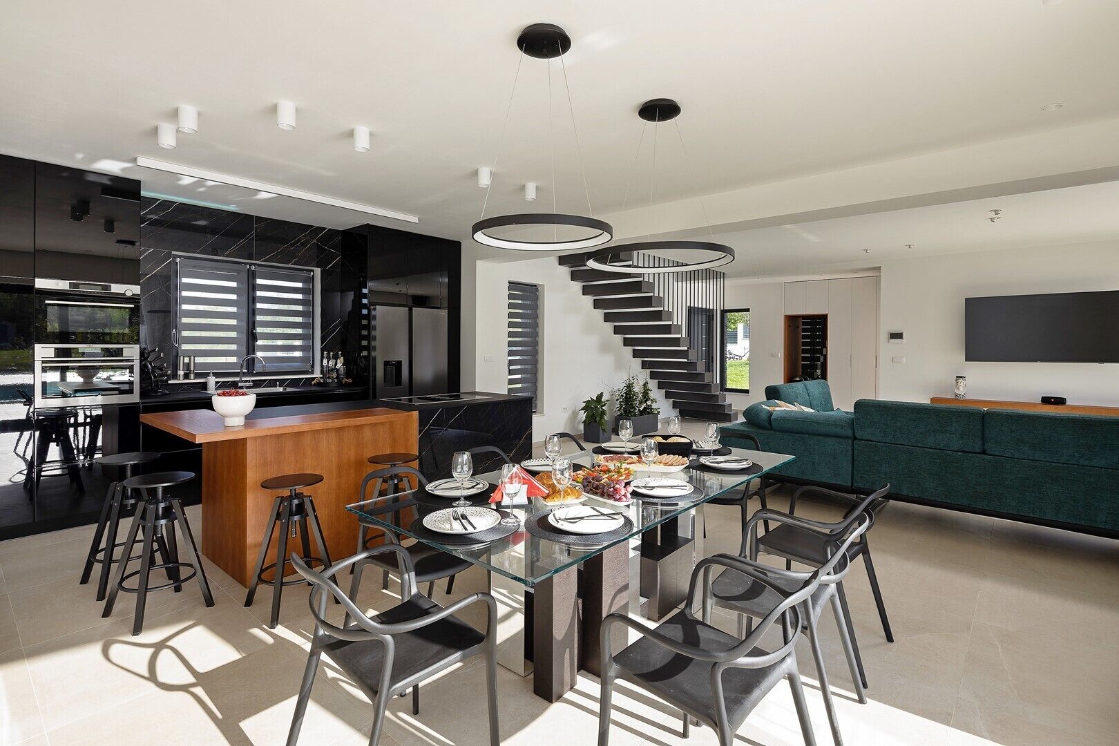 Una cuina moderna amb una illa central, una zona de menjador amb taula de vidre i una escala que porta a una sala d'estar.