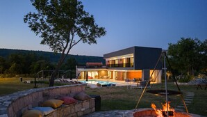 Een modern huis met een zwembad, buitenmeubilair en een vuurkorf.