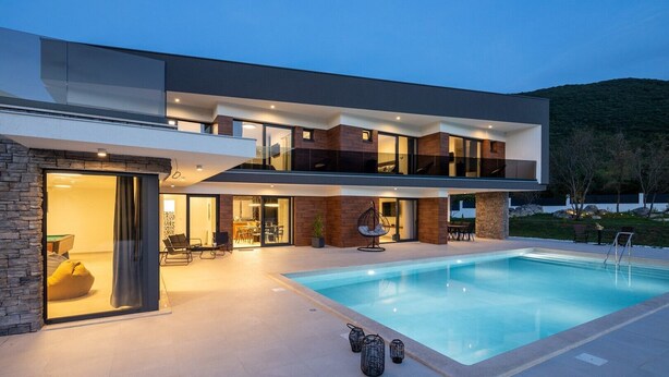 Een modern huis met twee verdiepingen, een zwembad, buitenmeubilair en een gevel van natuursteen.