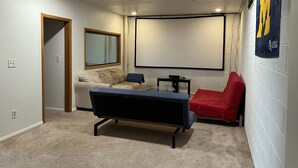 Una sala de cine en casa con proyector, un sofá, un sillón rojo y una pantalla grande.