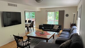 Una sala de estar con televisor, sofá, mesa de comedor y un amplio ventanal.