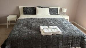 Una cama bien hecha con un edredón gris, almohadas blancas y una toalla blanca doblada sobre la cama.