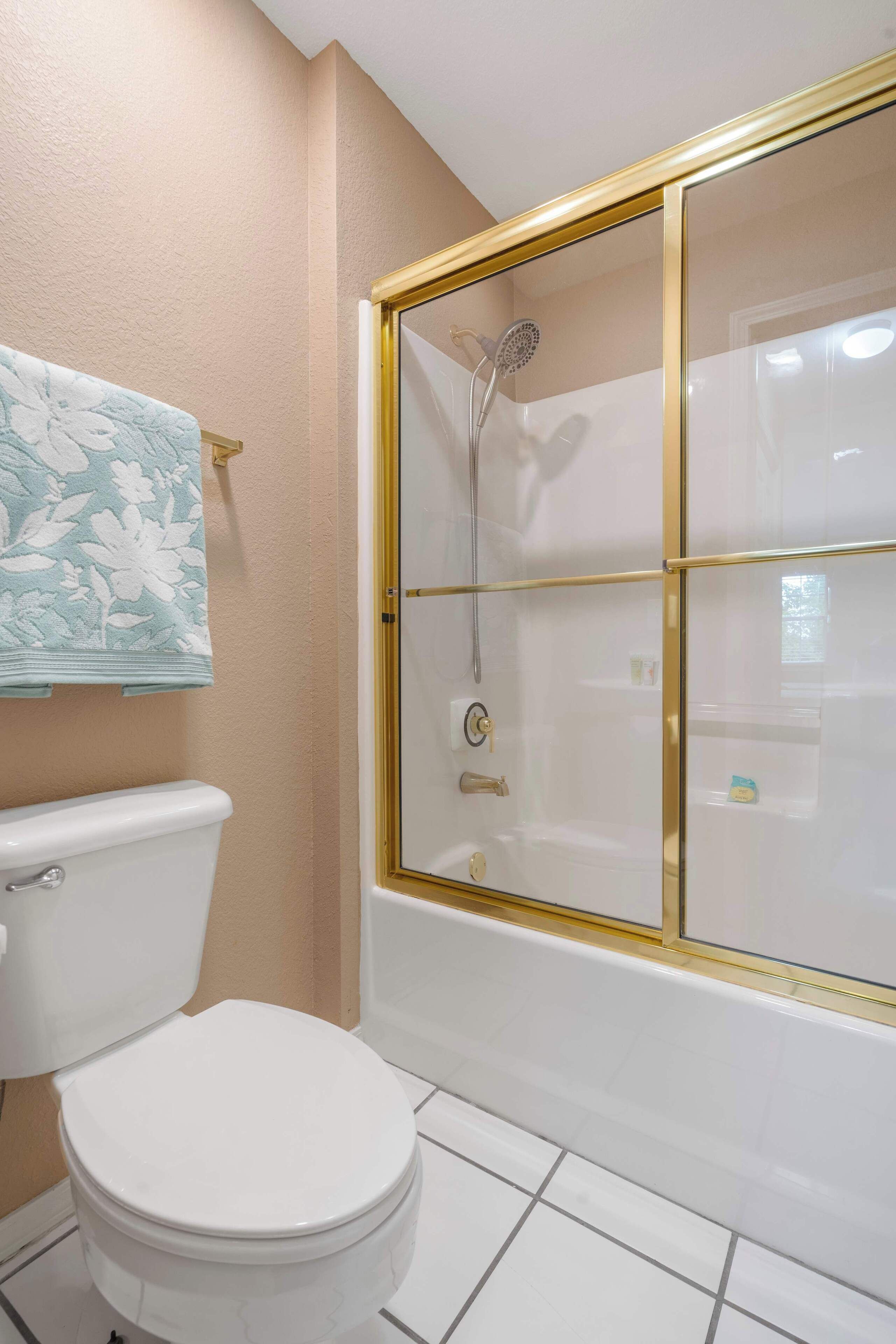 Un baño con inodoro, ducha con puerta de cristal y toalla con estampado floral.