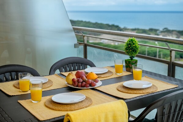 A table set with plates, glasses, and fruits, overlooking a scenic view.