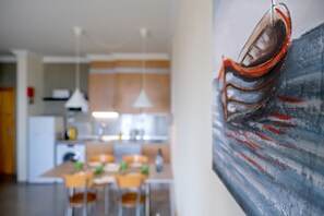 A modern kitchen with a dining area, a painting on the wall, and a dining table with chairs.