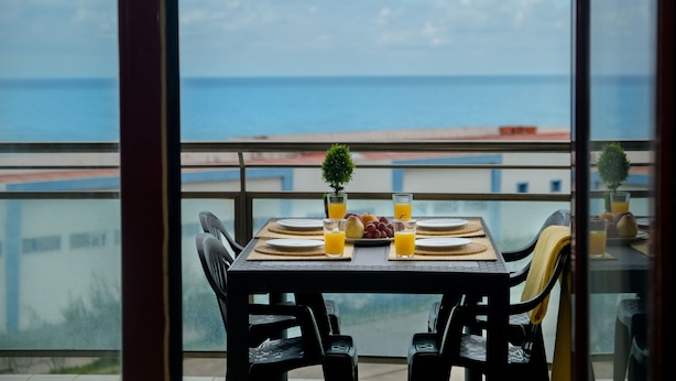 Une table à manger avec vue sur la mer, deux chaises et une petite plante en pot.