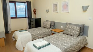 Une chambre d’hôtel avec deux lits, une fenêtre avec des rideaux, une petite table et des lampes fixées au mur.
