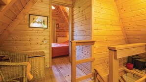 A cozy attic bedroom with wooden walls, a bed, a wicker chair, a small table, and a red chair. - Beautiful 3-bed House in Crni Lug (Delnice)