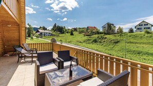 A balcony with wicker furniture and a glass table, overlooking a green landscape with houses. - Beautiful 3-bed House in Crni Lug (Delnice)