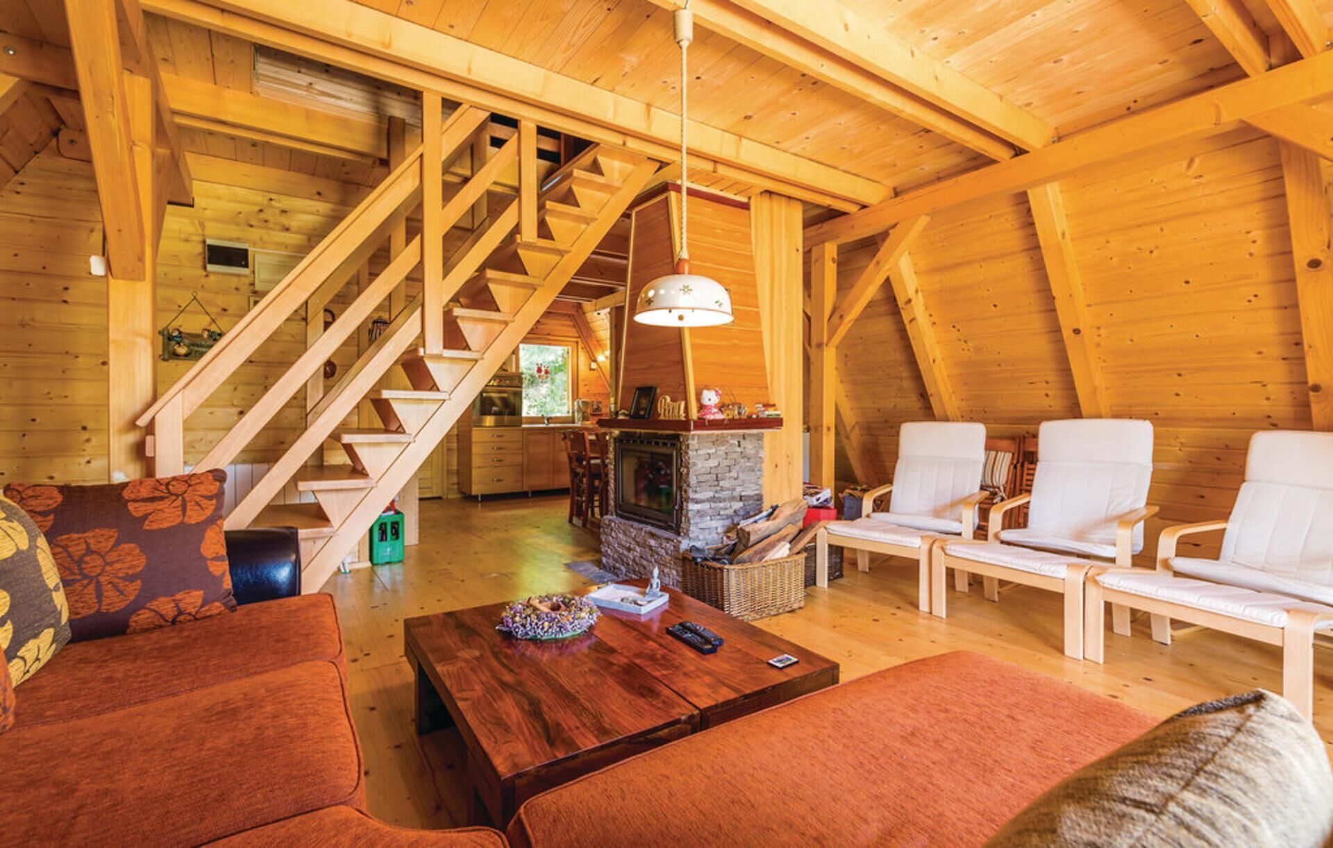 Un interior de madera con chimenea, sillas blancas, un sofá y una escalera.
