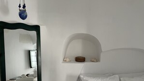 A bedroom with a bed, pillows, a mirror, and a shelf with decorative items. - Viletta Verte (Santorini)