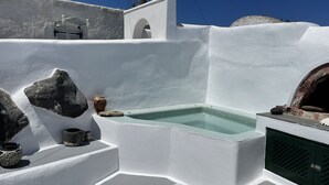 A white-walled outdoor area with a stone-tiled hot tub, a small stone oven, and a few decorative items. - Viletta Verte (Santorini)