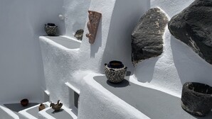 A white-walled interior with multiple ceramic pots and a stone wall. - Viletta Verte (Santorini)