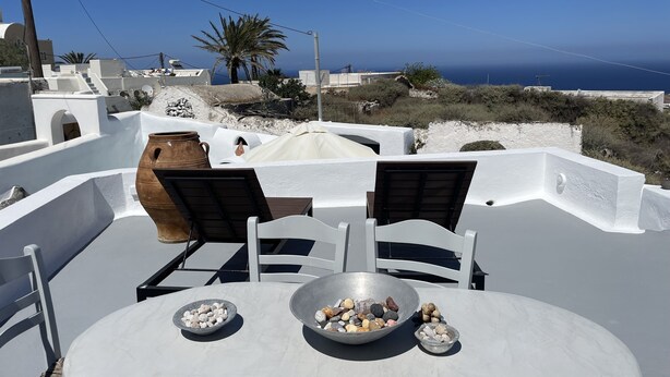 A rooftop terrace with a table, chairs, and a view of the sea. - Viletta Verte (Santorini)