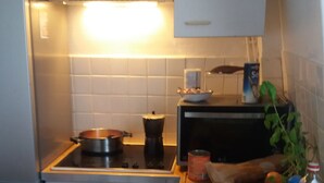 A compact kitchen with a refrigerator, stove, and a sink. There is a wooden countertop with various items like a plant, a bottle, and a can.