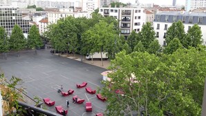 A view of a cityscape from a balcony with a parking lot, trees, and buildings in the background.