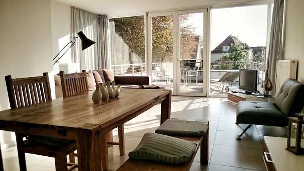 Een ruime woonkamer met een houten eettafel, een bank en een televisie op een dressoir.