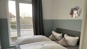 Een slaapkamer met een bed, kussens, een fotocollage aan de muur en uitzicht naar buiten door een raam.
