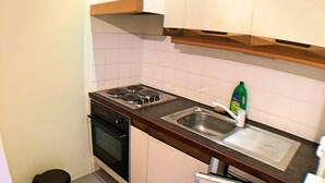 Una cocina compacta con gabinetes blancos, un lavamanos de acero inoxidable, una estufa y un pequeño cubo de basura.