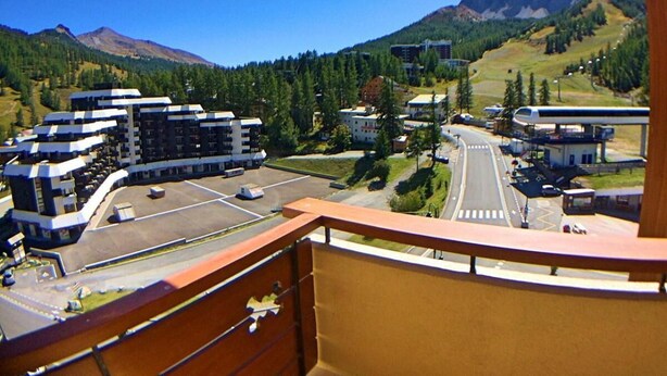 Vista desde un balcón sobre un estacionamiento, con edificios y una carretera que conduce a una montaña.